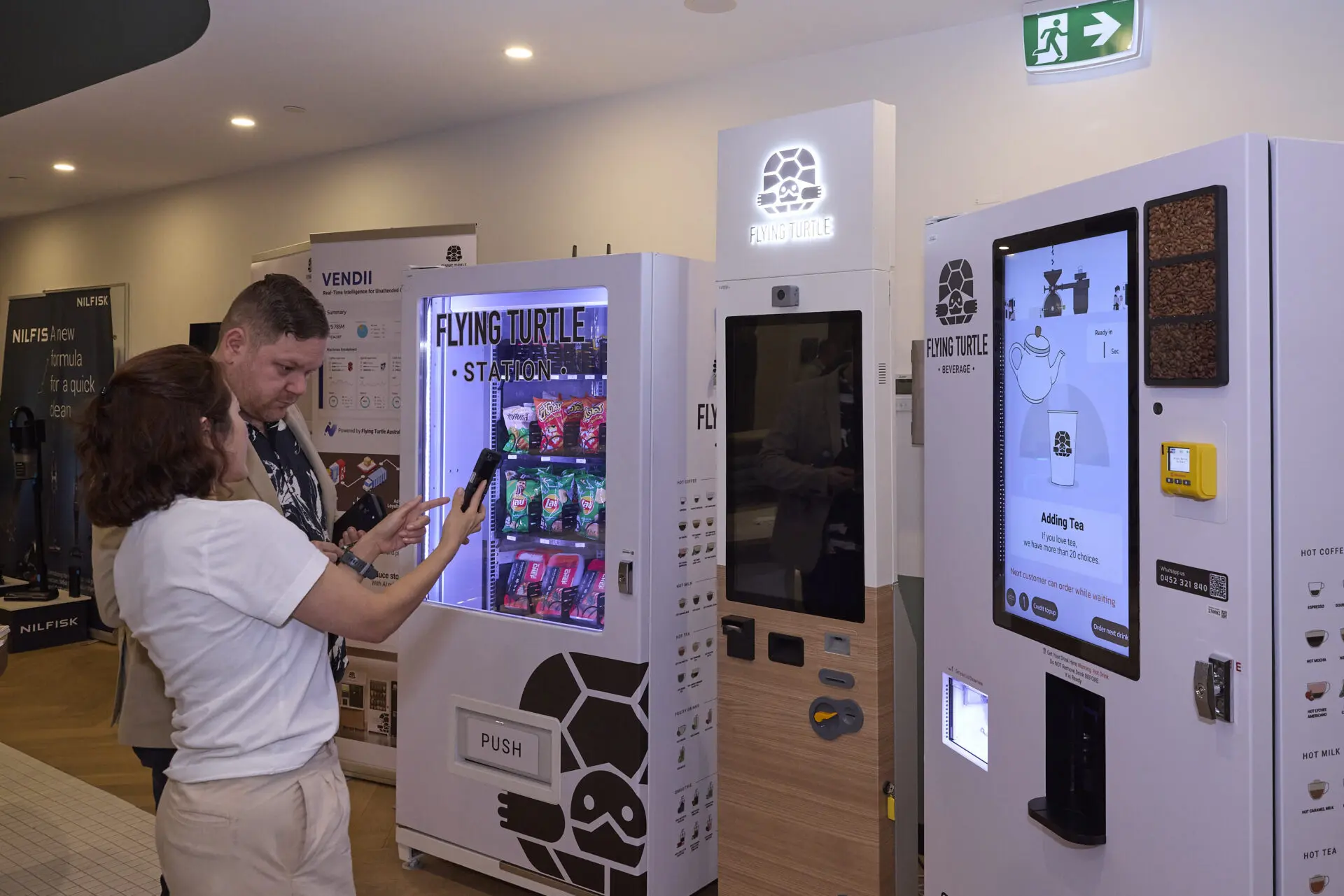 Two people chat in front of Flying Turtle Beverage Machines